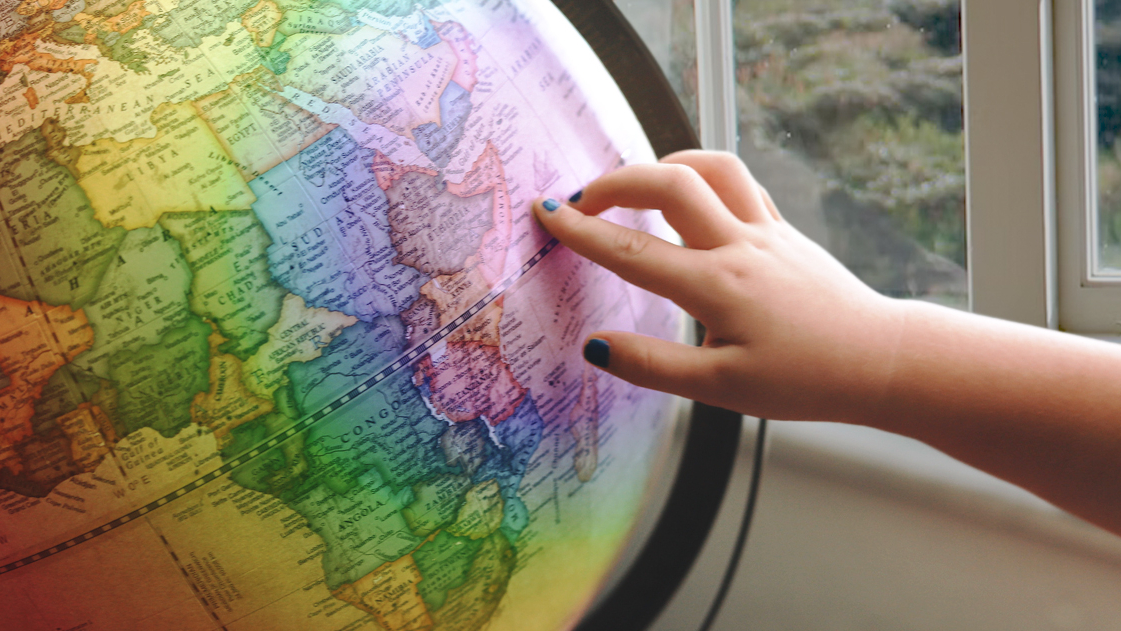 A hand pointing to a rainbow-coloured globe.