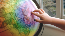 A hand pointing to a rainbow-coloured globe.