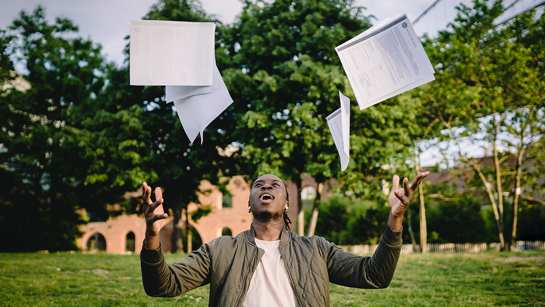 Academic goals achieved! A man throws his papers in the air.