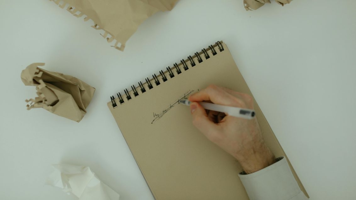 A man writing on a piece of paper then crossing it out indicating phrases to avoid in academic writing