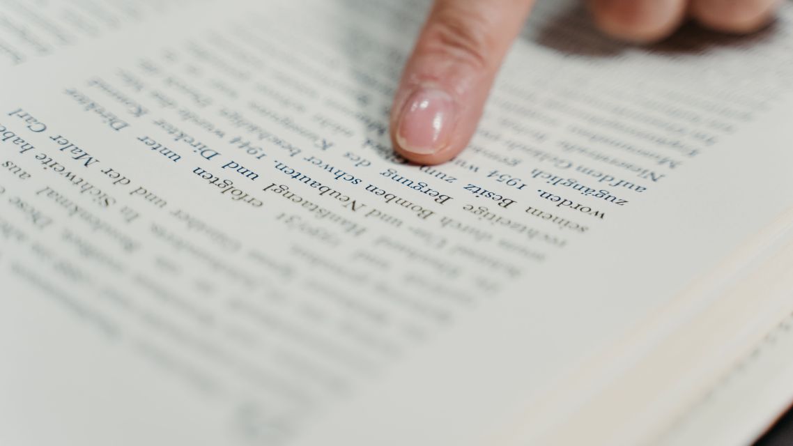 A finger pointing at text in a book.
