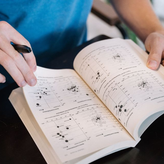 A man holding open a book containing research figures.