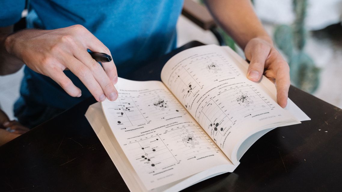 A man holding open a book containing research figures.