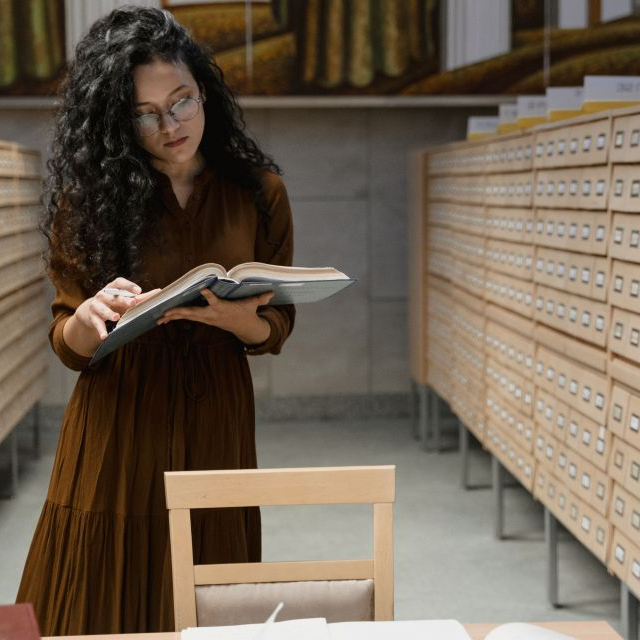 A woman looking at research and surrounded by file cabinets.